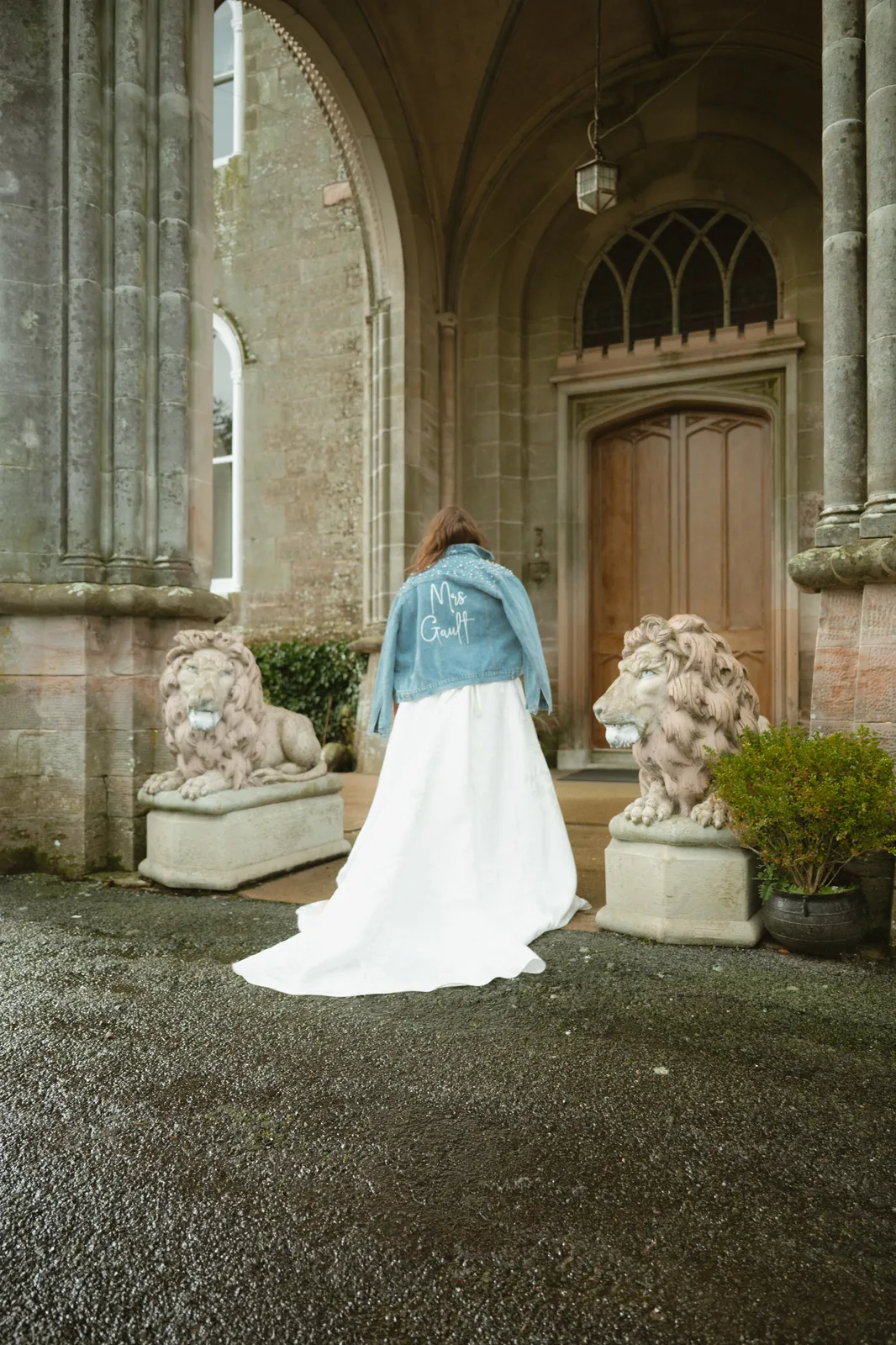 Leah and Keelan approach Killymoon Castle’s stone entrance, with her dress train trailing between the carved lions.
