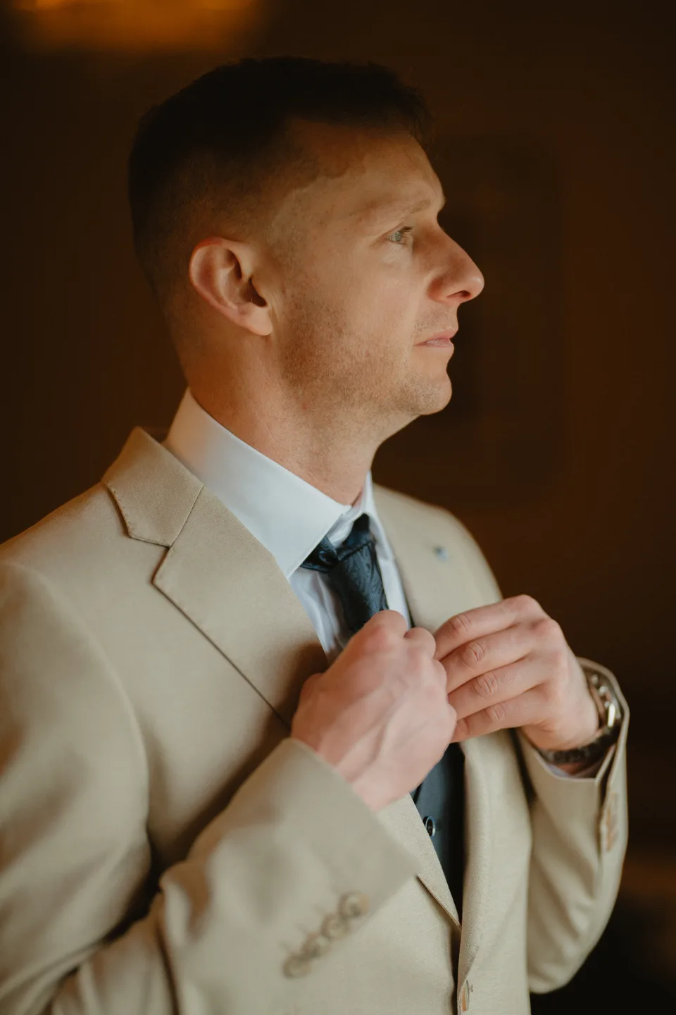 Jamie adjusting his tie by the window.