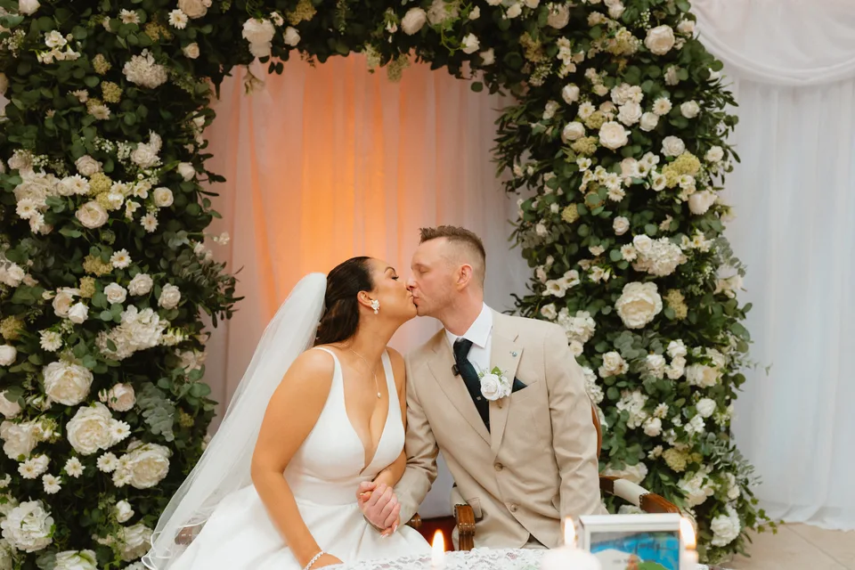 Lynsey and Jamie sharing a kiss beneath the ceremony flowers.
