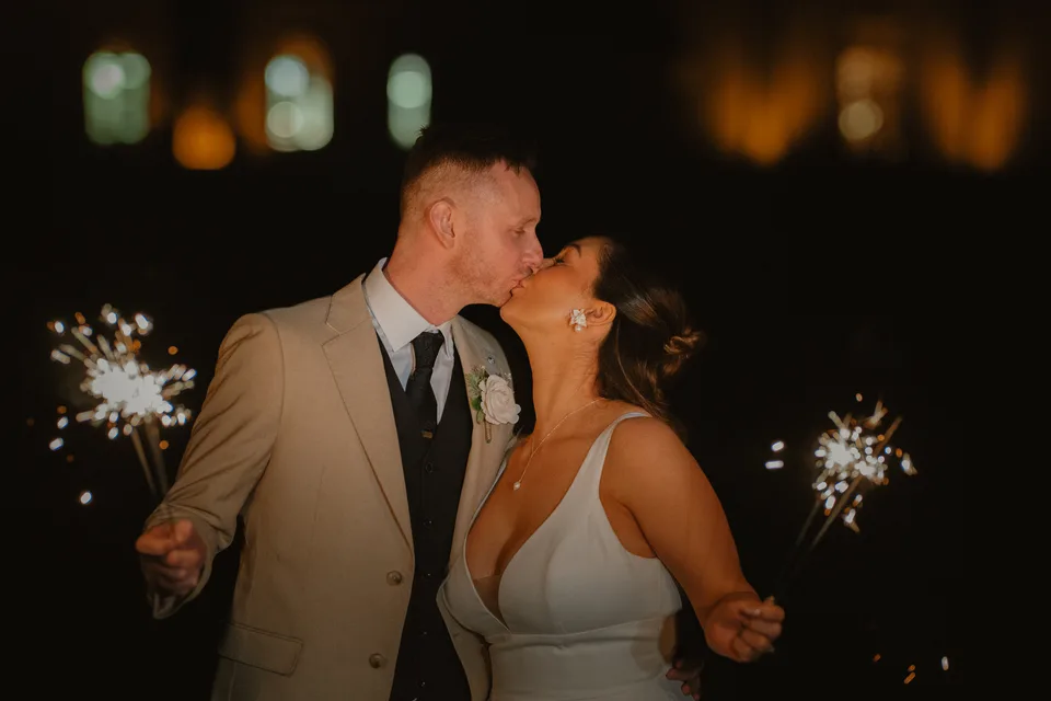 Lynsey and Jamie sharing a kiss with sparklers after dark.