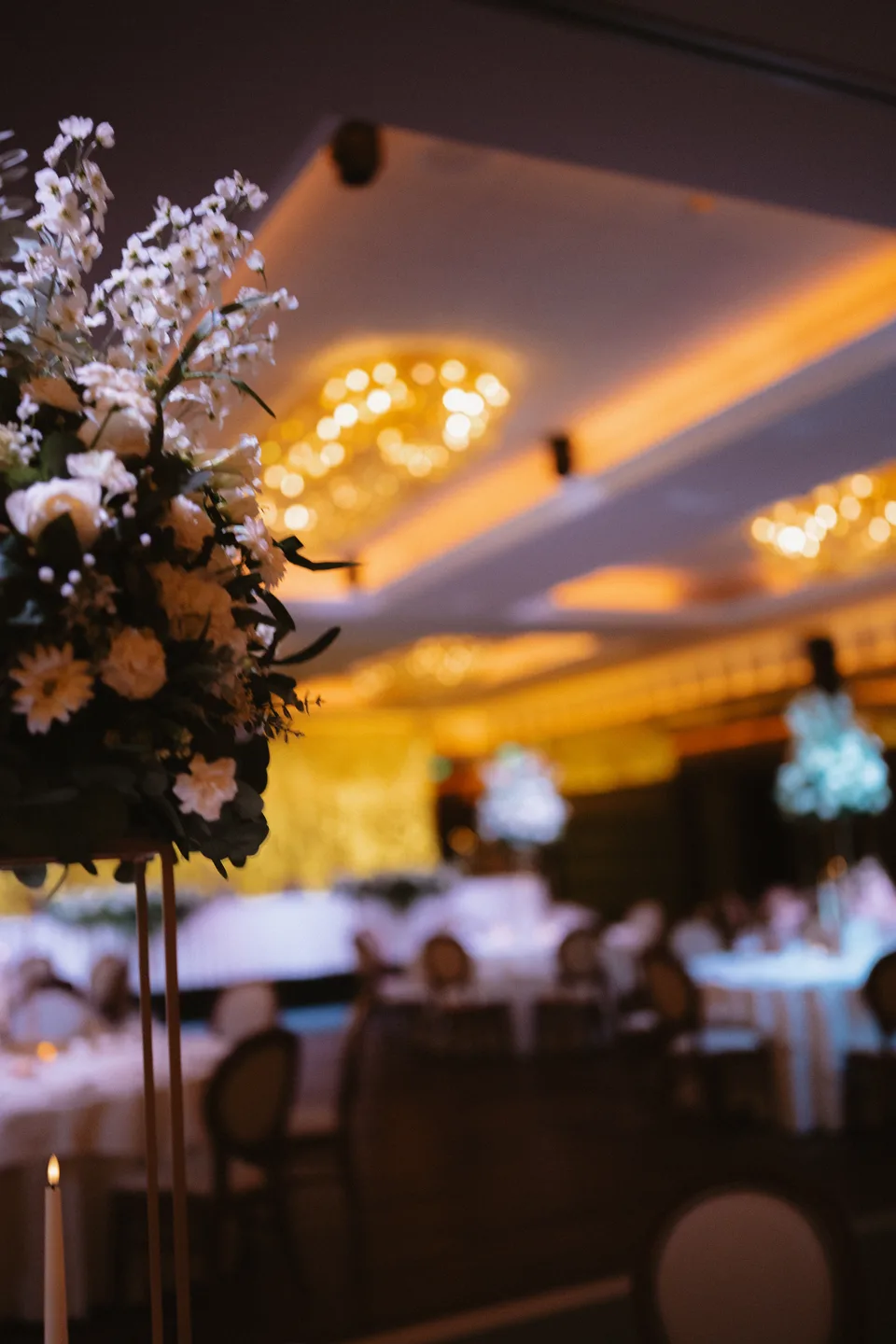 White flowers and warm chandelier light in the wedding reception room.