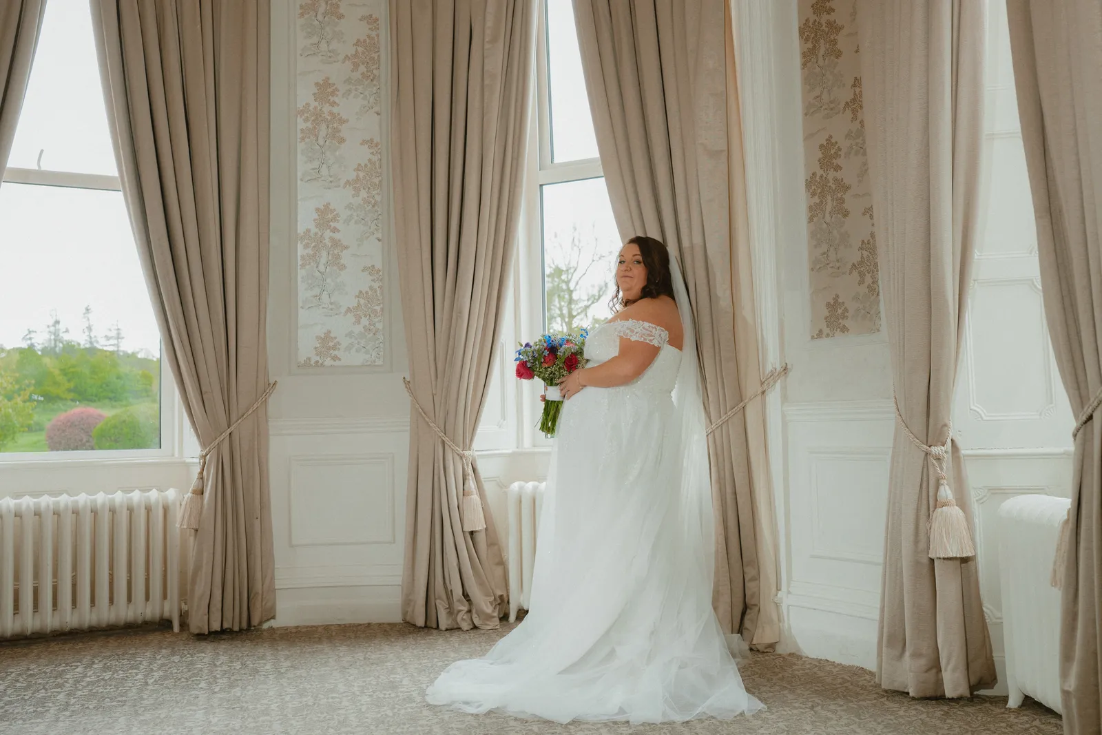 Michelle holding her bouquet by a tall window