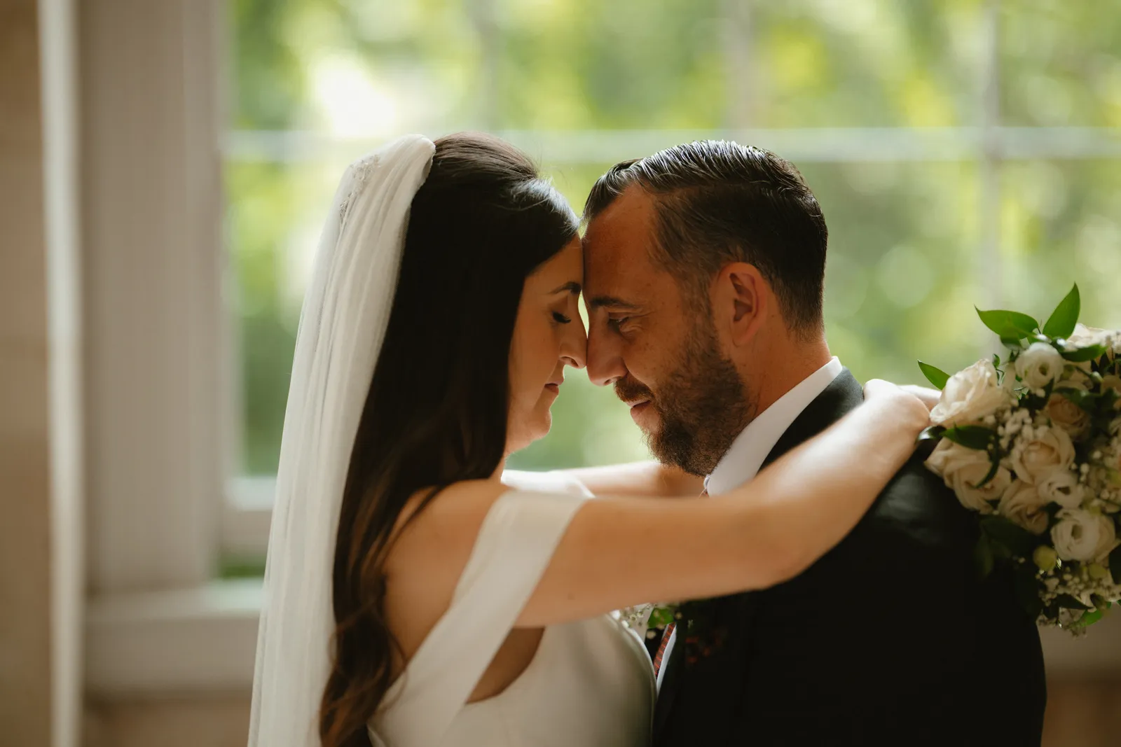 The couple embrace in window light