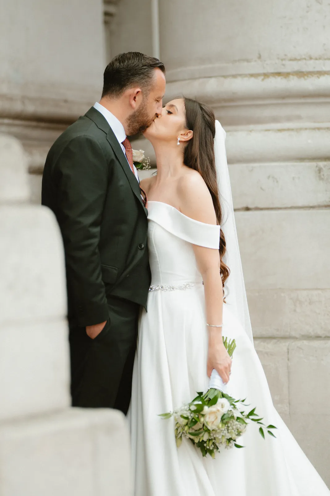The couple kiss beside a stone column