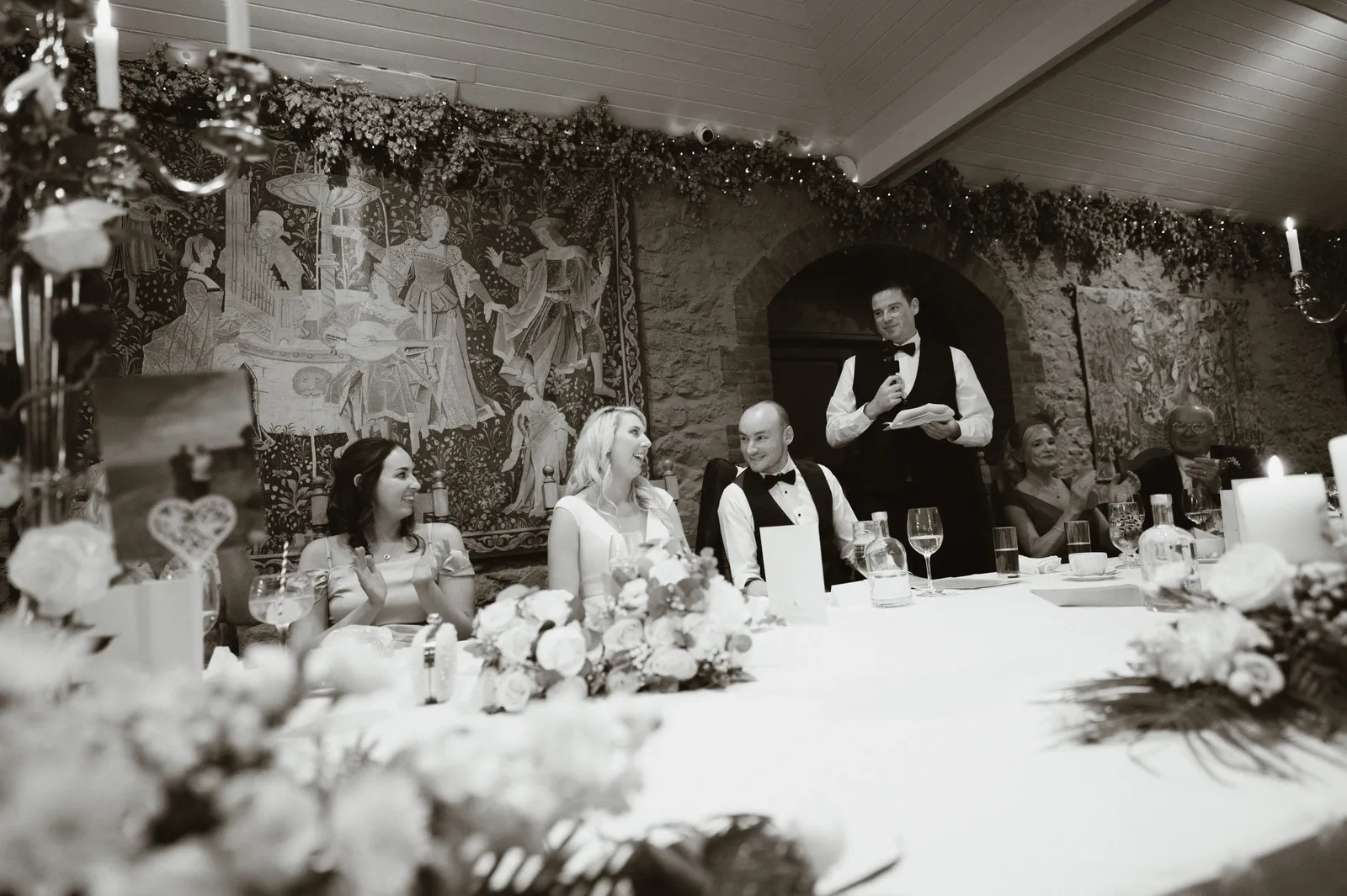 A guest reads a speech at the top table in Barberstown Castle’s stone reception room, with a tapestry behind him.