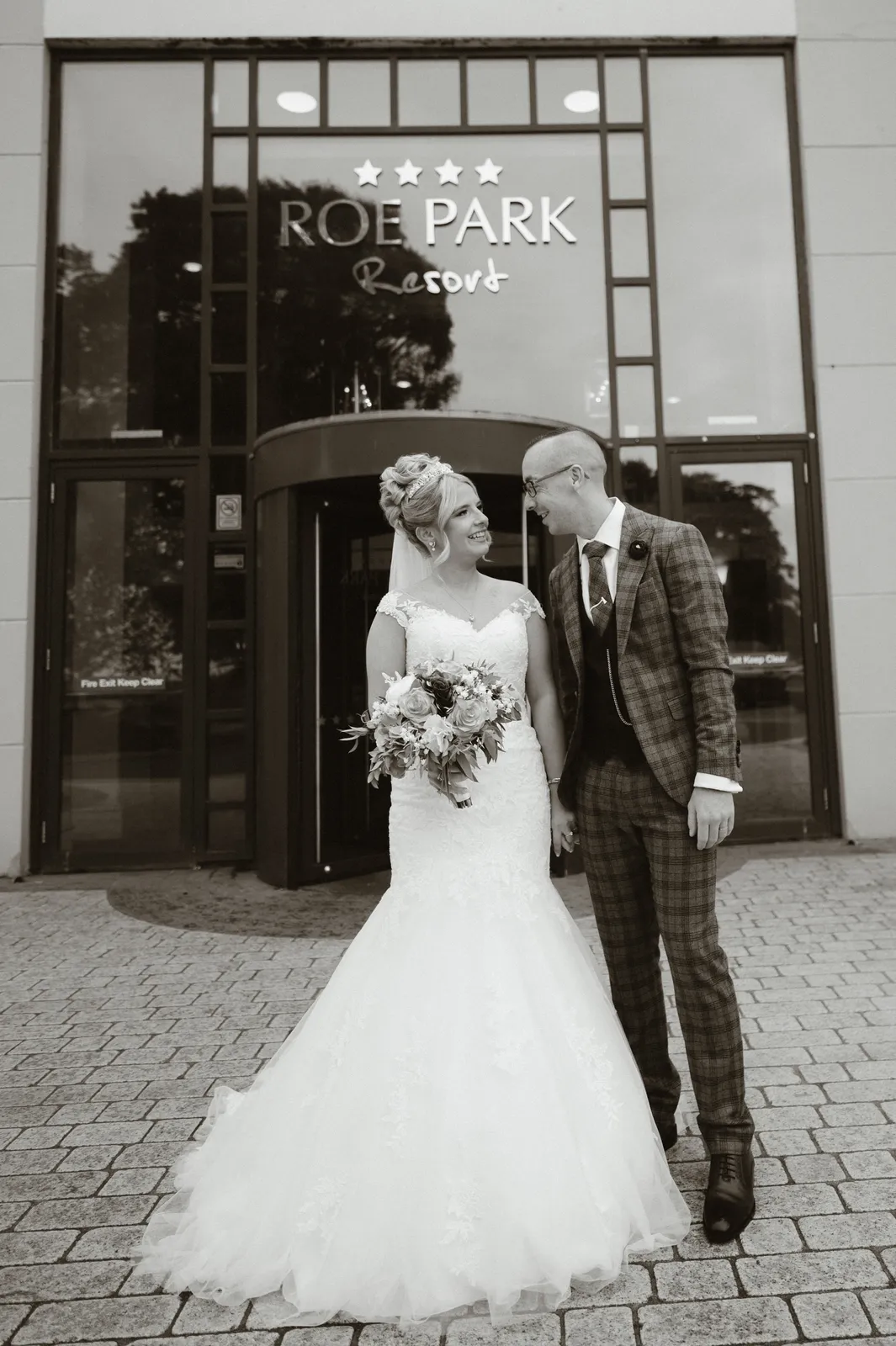 Tori and Wayne stand outside the glass entrance bearing the Roe Park Resort sign, in black and white.