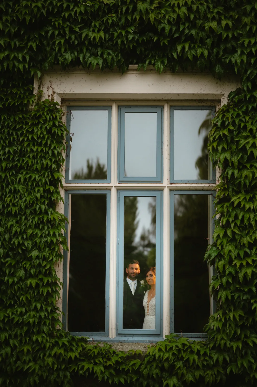 The couple framed by an ivy covered window